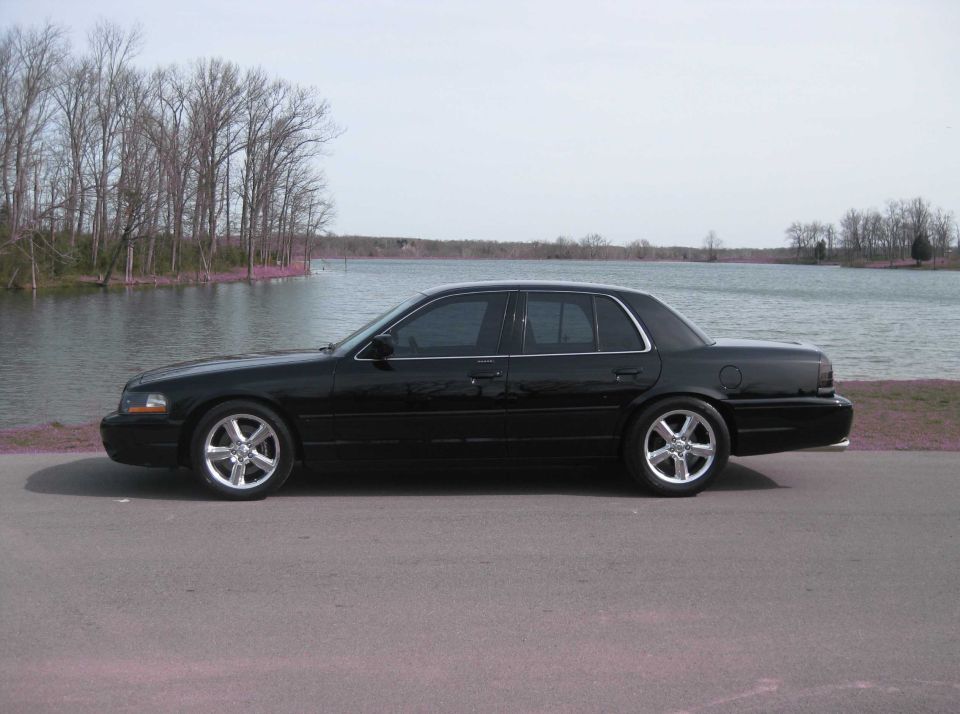 Side view of a black sedan parked by a lake.