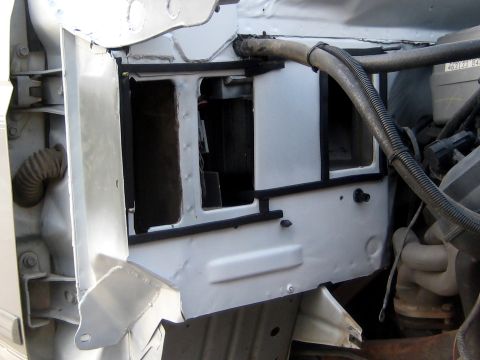 1996 Ford Bronco - A close-up view of the firewall area of a vehicle, showing exposed metal with black rubber seals around openings. Hoses and engine componen…