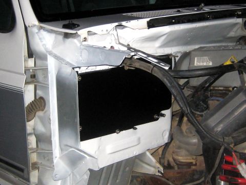 1996 Ford Bronco - Front fender removed from a white truck, exposing the bare-metal inner fender well and shock tower with fresh weld seams and reinforcement…