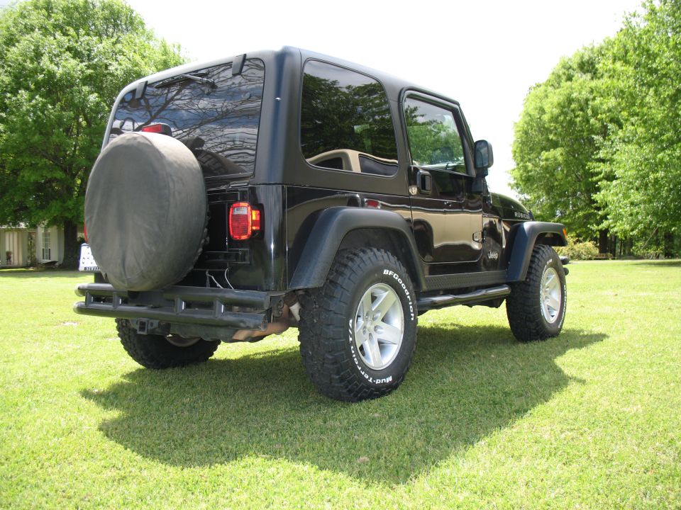 Black two-door Jeep Wrangler with spare tire parked on grass