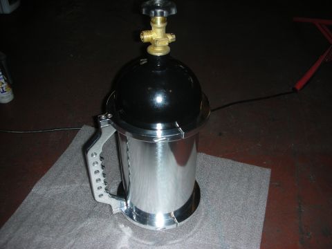 1992 Ford Crown Victoria - A black and chrome pressurized container with a brass valve sits on a gray mat on a dark floor. A red object is visible in the background.