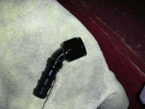 1992 Ford Crown Victoria - A black 90-degree AN fitting with barbed hose connection is shown resting on a light-colored towel. The fitting is angled upwards and to th…