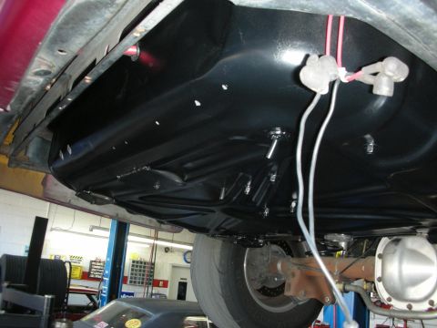 1992 Ford Crown Victoria - Underside view of a black fuel tank mounted to a vehicle frame, with wiring harness connected. The rear axle and part of a tire are also vi…
