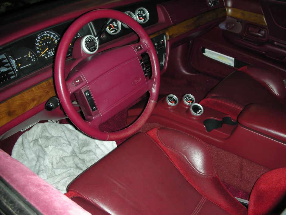 red interior of a car, showing steering wheel, dashboard gauges, and center console with extra gauges