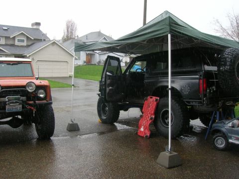 1996 Ford Bronco - Two Broncos are parked in a driveway under a green canopy during a rain shower.