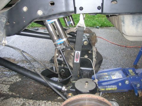 1996 Ford Bronco - Close-up of vehicle rear suspension components, including shocks and a strap, with a hydraulic jack visible.