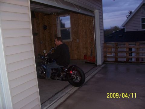 1988 Suzuki Samurai - A man rides a custom motorcycle out of a garage as dusk settles.