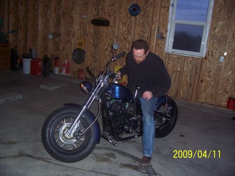 1988 Suzuki Samurai - A man sits on a blue motorcycle inside a garage with wood-paneled walls.