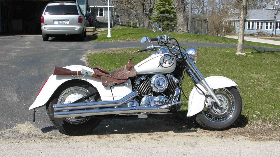 White cruiser motorcycle with a saddle seat parked on a driveway, silver minivan in background