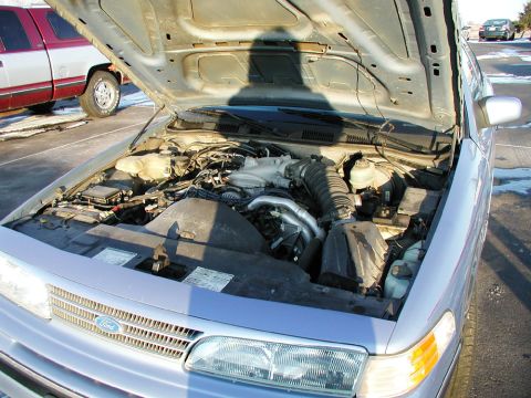 1993 Ford Crown Victoria - Engine bay of a 1993 Ford Crown Victoria, its V8 engine and front grille. Another vehicle is visible in the background.