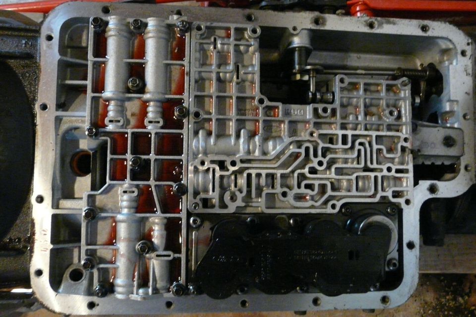 Automatic transmission valve body exposed with pan removed, showing solenoids and red ATF residue
