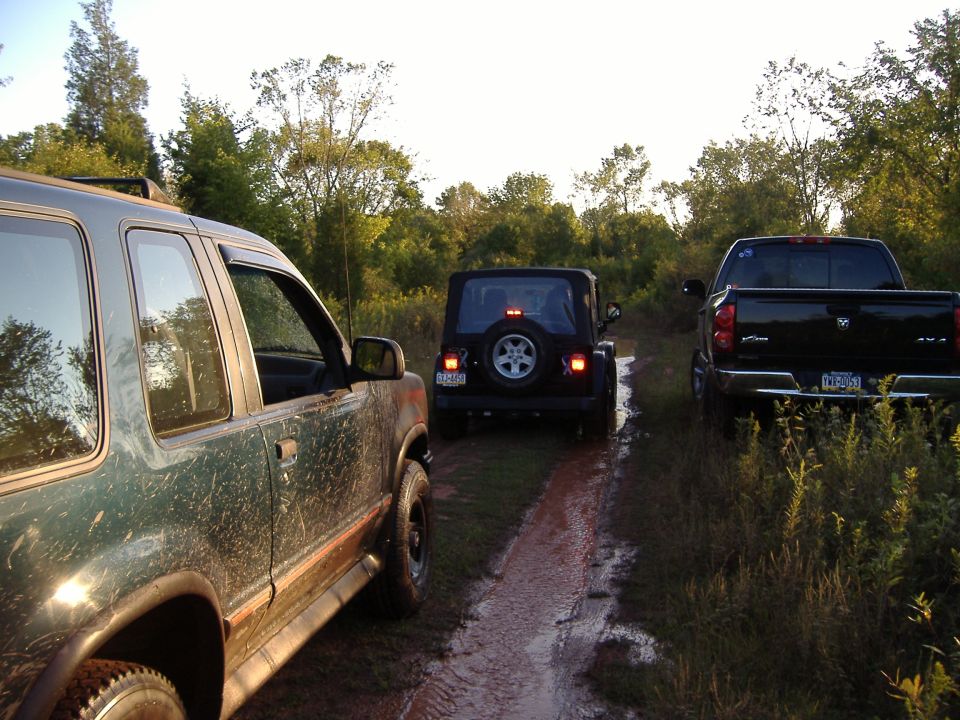 Green SUV, black Jeep, and black Dodge Ram truck on a muddy trail