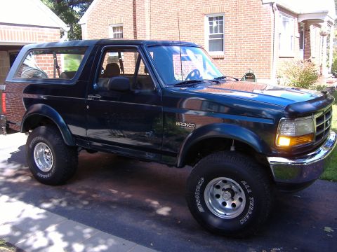 1995 Ford Bronco - A dark blue 1995 Ford Bronco is parked in a driveway in front of a brick house.