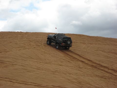 1994 Ford Bronco - A black SUV navigates a sandy terrain, leaving tire tracks behind as it ascends a dune.
