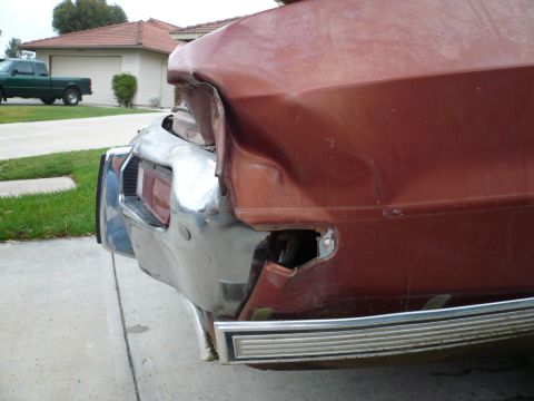1975 Ford Ranchero - Rear view of a damaged red pickup truck with a bent chrome bumper and missing taillight.
