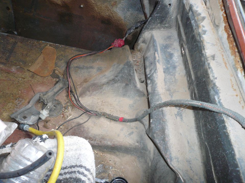 Close-up of vehicle's interior floor with exposed wiring and a yellow hose