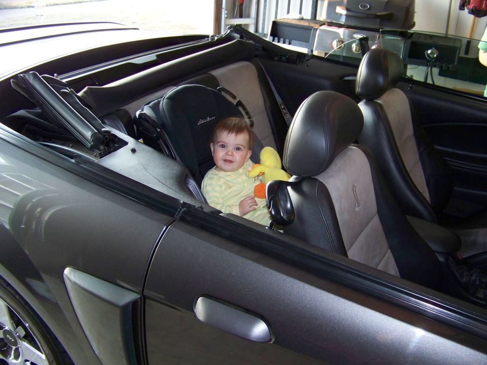 Baby in car seat inside gray convertible with top down in a garage