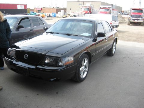 2003 Ford Crown Victoria - A black Mercury Grand Marquis is parked in an outdoor lot, with other vehicles and buildings visible.