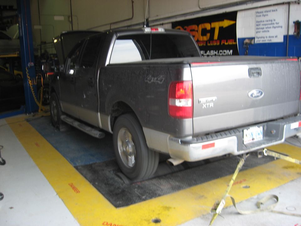 Rear view of a dark gray Ford F-150 XTR pickup truck on a dynamometer. The truck has a two-tone paint scheme with a silver lower body