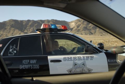 1991 Ford LTD Crown Victoria - Side view of a sheriff's patrol car driving in a desert landscape.