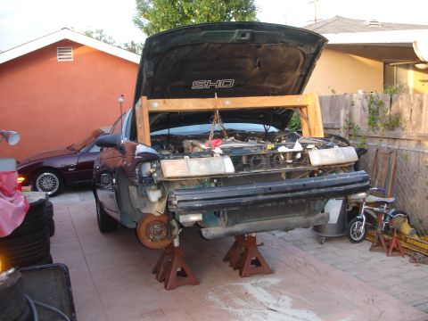 1995 Ford Taurus - Front end of a 1995 Ford Taurus SHO undergoing engine work, with a wooden support beam in place.