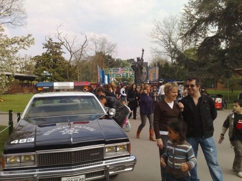 1991 Ford Crown Victoria - A police car is parked in front of a crowd of people, with a statue visible in the distance.