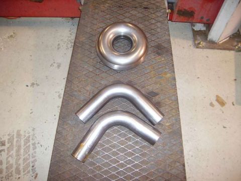 1969 MINI Cooper - A collection of exhaust pipe components, including a circular connector and two U-shaped bends, are laid out on a textured surface.