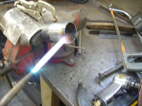 1969 MINI Cooper - A metal pipe is being cut with a torch while secured in a vise, with various tools scattered around.