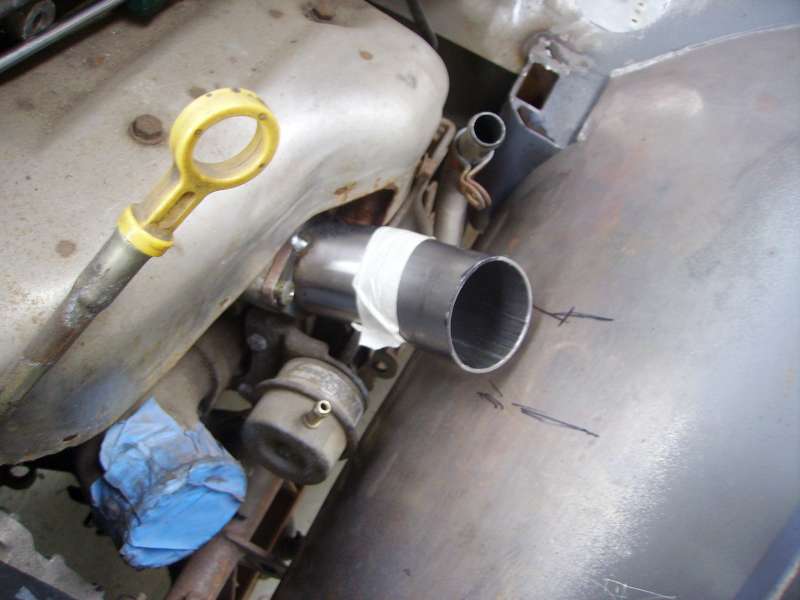 Close-up of a metal exhaust pipe being fitted with a new section, taped in place. Oil dipstick visible
