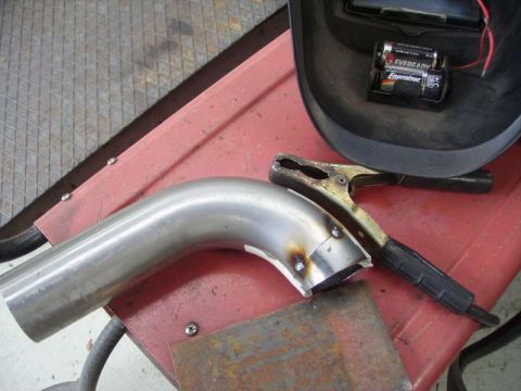 1969 MINI Cooper - A close-up view of a metal exhaust pipe being prepared for welding, alongside welding equipment.