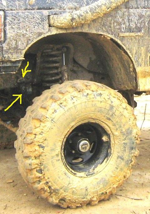 1990 Ford Bronco - Close-up of a muddy off-road tire and suspension system, showing wear and tear.