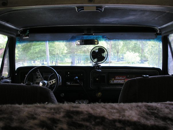 Interior view of a vehicle, showing dashboard, steering wheel, and seats. A small fan is mounted on the dash