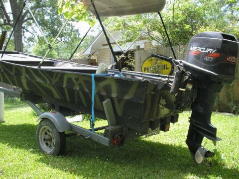 1979 Ford Bronco - A camouflaged boat with a Mercury 40 outboard motor is parked on a trailer in a grassy yard.