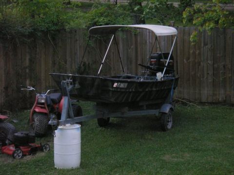 1979 Ford Bronco - A boat with a canopy and outboard motor sits on a trailer in a grassy yard.