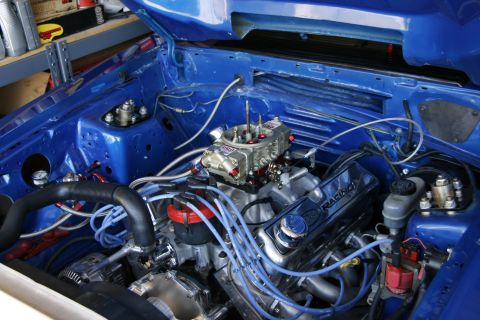 1989 Ford Mustang - Engine bay of a 1989 Ford Mustang features a V8 engine with a prominent carburetor and vibrant blue paint.