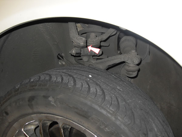 Suspension ball joint and control arm behind a tire, with white arrow indicator