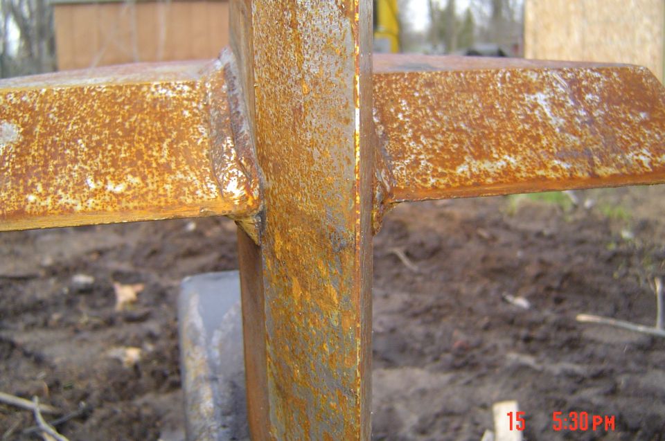 Close-up of rusty welded steel joint joining a vertical bar to horizontal angle-iron rails