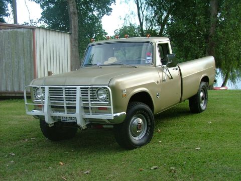 1975 International Scout II - This International pickup truck has a white grille guard and is parked on a grassy area near trees and water.