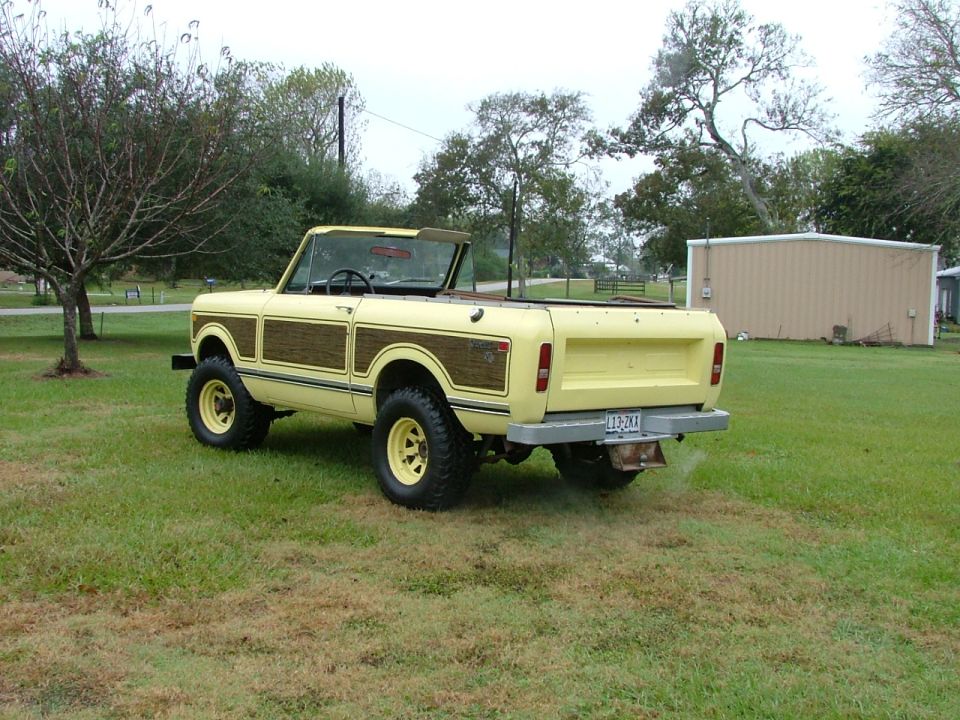 Yellow 1975 International Scout II convertible SUV with wood paneling, rear 3/4 view, parked on grass