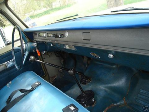 1975 International Scout II - The interior of a vehicle shows blue seats, a dashboard with a radio, and a floor shifter.