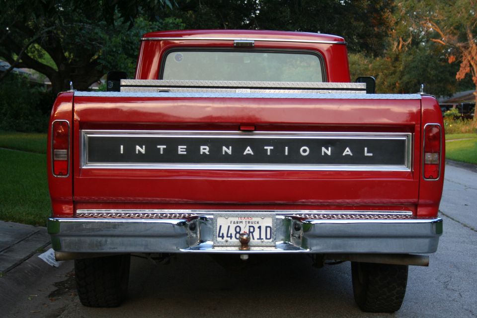 Red pickup truck rear with INTERNATIONAL tailgate badge and Texas Farm Truck license plate