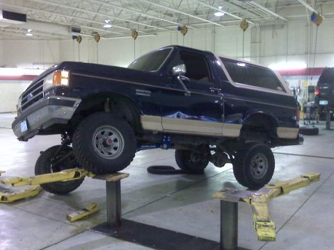 1990 Ford Bronco - This Ford Bronco is raised on a lift, showing its suspension and undercarriage in a workshop setting.
