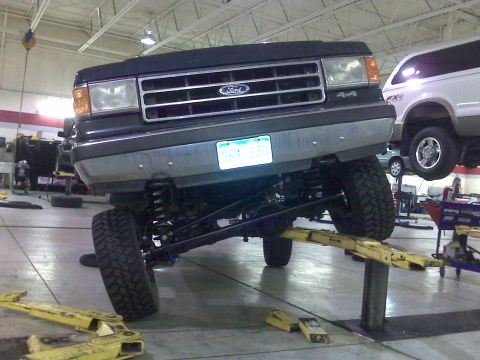 1990 Ford Bronco - A modified Ford Bronco is raised on a hydraulic lift in a garage, showing its custom suspension.