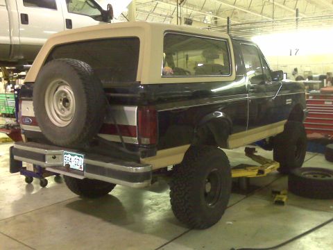 1990 Ford Bronco - Rear view of a 1990 Ford Bronco with a tan top, raised on a service lift.