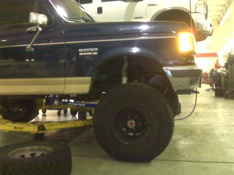 1990 Ford Bronco - A blue 1990 Ford Bronco is raised on a lift, revealing its suspension and large off-road tires.