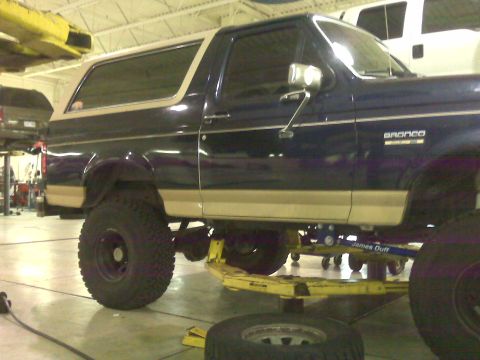 1990 Ford Bronco - A dark blue 1990 Ford Bronco with tan trim is shown on a lift in a garage.