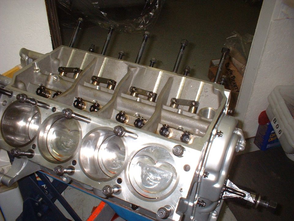 Aluminum engine block with four cylinders visible, showing pistons and valve train components