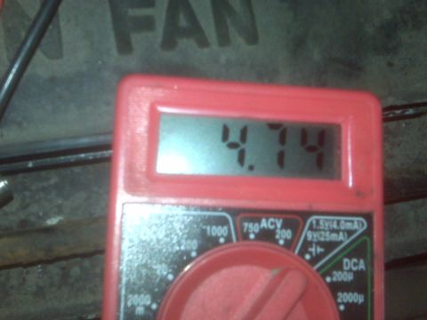 1995 Ford Bronco - A red digital multimeter displays a reading of 4.74. The multimeter is positioned in front of a dark, textured surface with the partial wor…