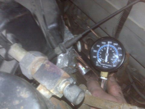 1995 Ford Bronco - A close-up view of a compression tester gauge attached to an engine component. The gauge shows a reading between 120 and 150 psi, with the…