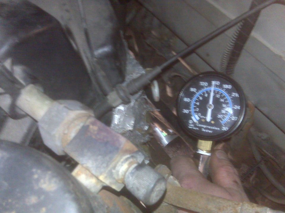 Compression tester gauge on an engine, reading around 140 psi.